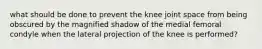 what should be done to prevent the knee joint space from being obscured by the magnified shadow of the medial femoral condyle when the lateral projection of the knee is performed?