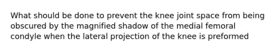 What should be done to prevent the knee joint space from being obscured by the magnified shadow of the medial femoral condyle when the lateral projection of the knee is preformed