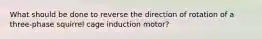 What should be done to reverse the direction of rotation of a three-phase squirrel cage induction motor?