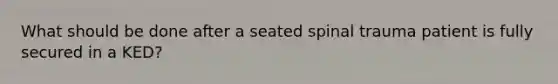 What should be done after a seated spinal trauma patient is fully secured in a KED?