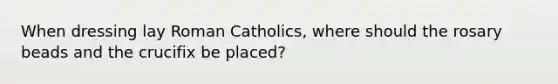 When dressing lay Roman Catholics, where should the rosary beads and the crucifix be placed?