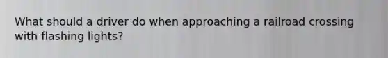 What should a driver do when approaching a railroad crossing with flashing lights?