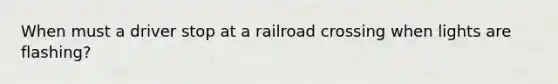 When must a driver stop at a railroad crossing when lights are flashing?