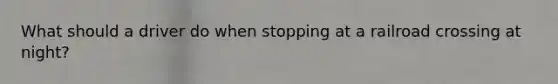 What should a driver do when stopping at a railroad crossing at night?