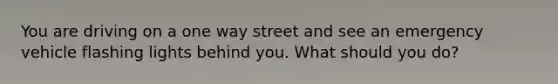 You are driving on a one way street and see an emergency vehicle flashing lights behind you. What should you do?