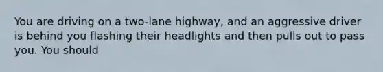 You are driving on a two-lane highway, and an aggressive driver is behind you flashing their headlights and then pulls out to pass you. You should