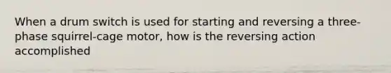 When a drum switch is used for starting and reversing a three-phase squirrel-cage motor, how is the reversing action accomplished