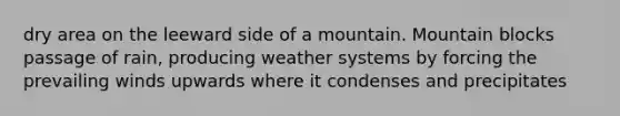 dry area on the leeward side of a mountain. Mountain blocks passage of rain, producing weather systems by forcing the prevailing winds upwards where it condenses and precipitates