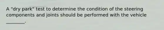 A "dry park" test to determine the condition of the steering components and joints should be performed with the vehicle ________.