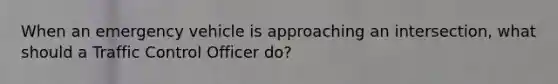 When an emergency vehicle is approaching an intersection, what should a Traffic Control Officer do?