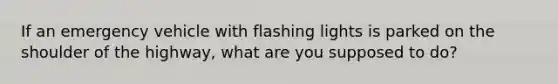 If an emergency vehicle with flashing lights is parked on the shoulder of the highway, what are you supposed to do?