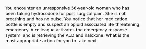 You encounter an unresponsive 56-year-old woman who has been taking hydrocodone for post surgical pain. She is not breathing and has no pulse. You notice that her medication bottle is empty and suspect an opioid associated life-threatening emergency. A colleague activates the emergency response system, and is retrieving the AED and naloxone. What is the most appropriate action for you to take next