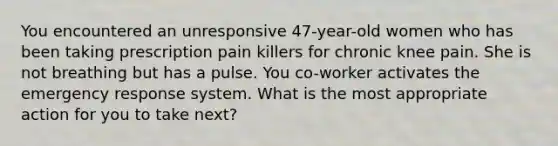 You encountered an unresponsive 47-year-old women who has been taking prescription pain killers for chronic knee pain. She is not breathing but has a pulse. You co-worker activates the emergency response system. What is the most appropriate action for you to take next?