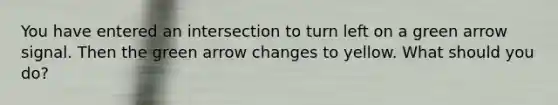 You have entered an intersection to turn left on a green arrow signal. Then the green arrow changes to yellow. What should you do?