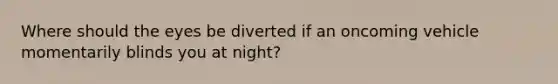 Where should the eyes be diverted if an oncoming vehicle momentarily blinds you at night?