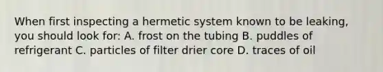 When first inspecting a hermetic system known to be leaking, you should look for: A. frost on the tubing B. puddles of refrigerant C. particles of filter drier core D. traces of oil