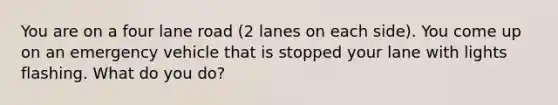 You are on a four lane road (2 lanes on each side). You come up on an emergency vehicle that is stopped your lane with lights flashing. What do you do?