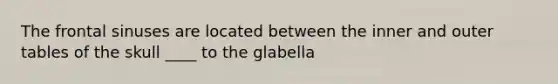 The frontal sinuses are located between the inner and outer tables of the skull ____ to the glabella