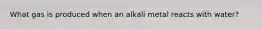 What gas is produced when an alkali metal reacts with water?