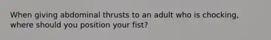 When giving abdominal thrusts to an adult who is chocking, where should you position your fist?