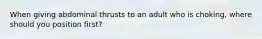 When giving abdominal thrusts to an adult who is choking, where should you position first?