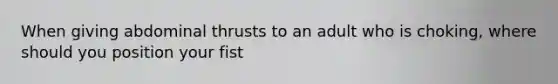 When giving abdominal thrusts to an adult who is choking, where should you position your fist