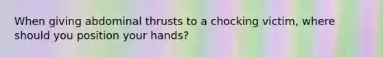 When giving abdominal thrusts to a chocking victim, where should you position your hands?