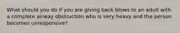 What should you do if you are giving back blows to an adult with a complete airway obstruction who is very heavy and the person becomes unresponsive?