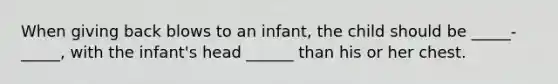 When giving back blows to an infant, the child should be _____-_____, with the infant's head ______ than his or her chest.