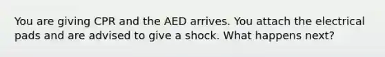 You are giving CPR and the AED arrives. You attach the electrical pads and are advised to give a shock. What happens next?