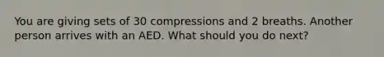 You are giving sets of 30 compressions and 2 breaths. Another person arrives with an AED. What should you do next?