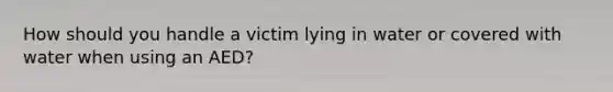 How should you handle a victim lying in water or covered with water when using an AED?