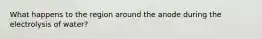 What happens to the region around the anode during the electrolysis of water?
