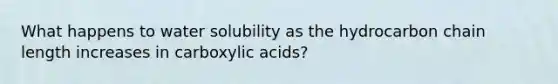 What happens to water solubility as the hydrocarbon chain length increases in carboxylic acids?