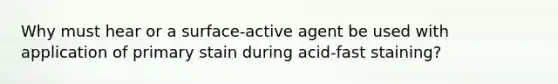 Why must hear or a surface-active agent be used with application of primary stain during acid-fast staining?