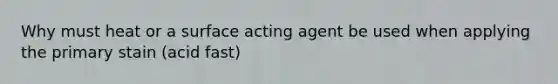 Why must heat or a surface acting agent be used when applying the primary stain (acid fast)