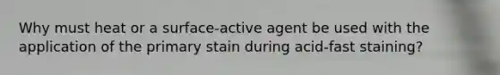 Why must heat or a surface-active agent be used with the application of the primary stain during acid-fast staining?