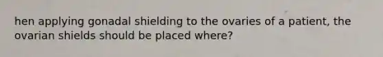 hen applying gonadal shielding to the ovaries of a patient, the ovarian shields should be placed where?