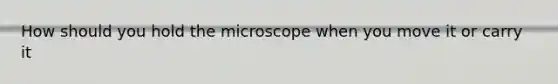 How should you hold the microscope when you move it or carry it