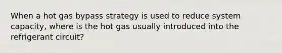 When a hot gas bypass strategy is used to reduce system capacity, where is the hot gas usually introduced into the refrigerant circuit?