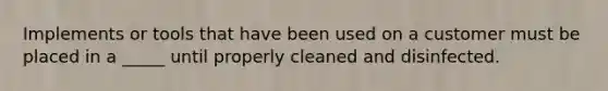 Implements or tools that have been used on a customer must be placed in a _____ until properly cleaned and disinfected.