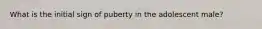 What is the initial sign of puberty in the adolescent male?