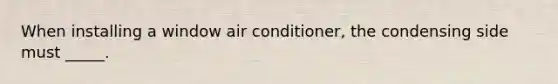 When installing a window air conditioner, the condensing side must _____.