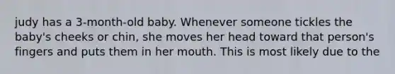 judy has a 3-month-old baby. Whenever someone tickles the baby's cheeks or chin, she moves her head toward that person's fingers and puts them in her mouth. This is most likely due to the