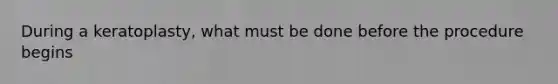 During a keratoplasty, what must be done before the procedure begins