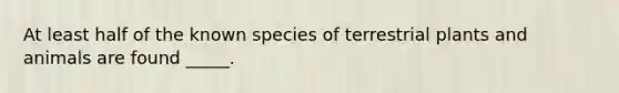 At least half of the known species of terrestrial plants and animals are found _____.