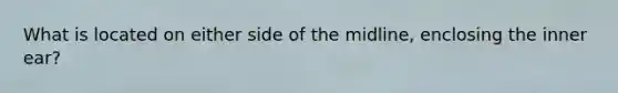 What is located on either side of the midline, enclosing the inner ear?
