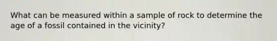 What can be measured within a sample of rock to determine the age of a fossil contained in the vicinity?