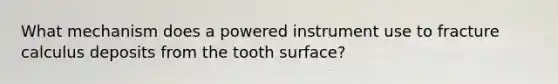 What mechanism does a powered instrument use to fracture calculus deposits from the tooth surface?