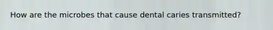 How are the microbes that cause dental caries transmitted?